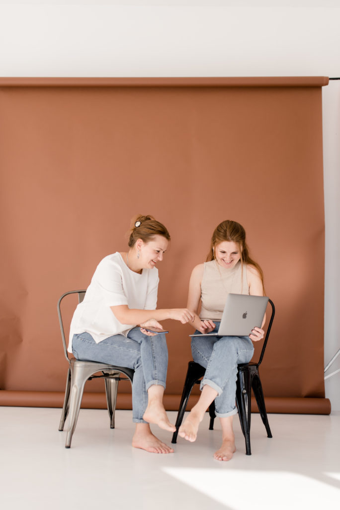 Zwei Frauen auf Stühlen vor Laptop, Community